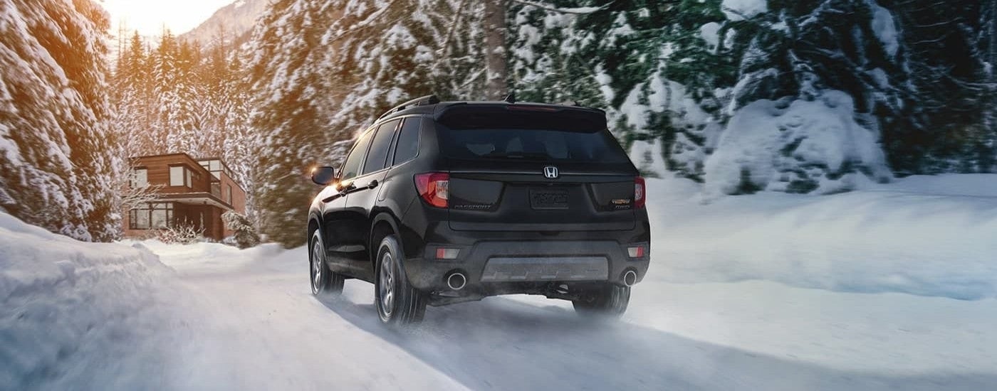 A black rear-facing 2023 Honda Passport TrailSport driving in snow.