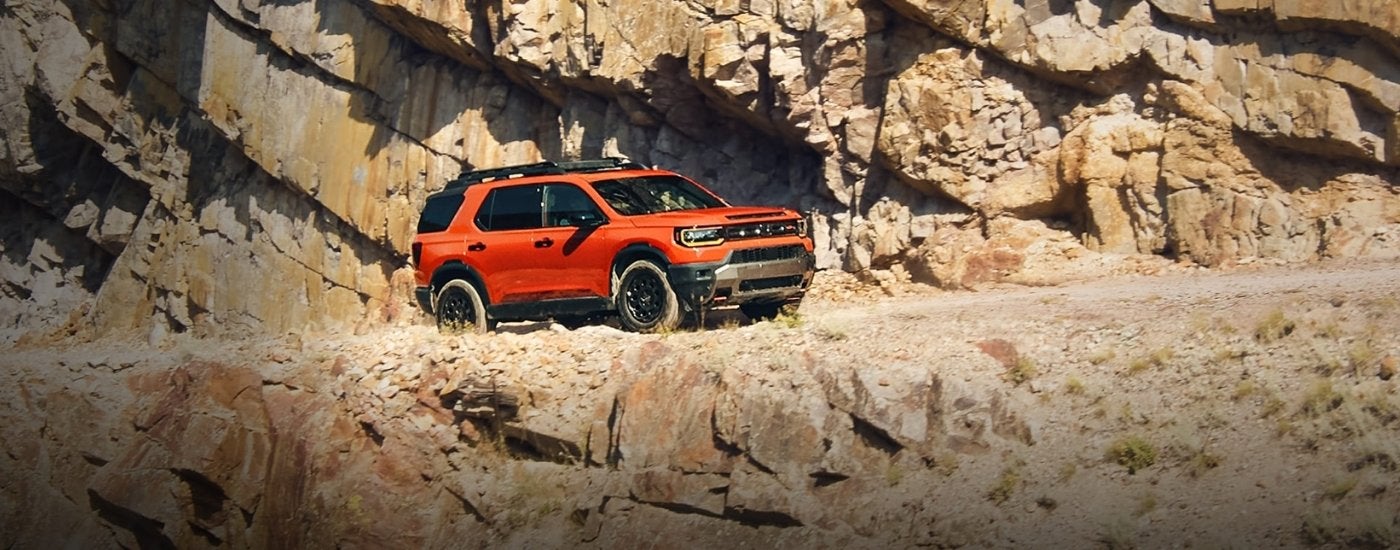 An orange 2026 Honda Passport Elite TrailSport driving a rocky road.