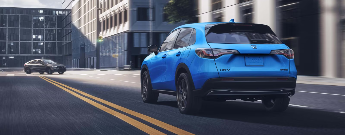 A blue 2027 Honda HR-V driving down a road rear-facing.