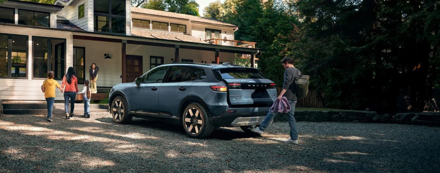 A blue 2024 Honda Prologue Elite is shown from the rear parked near a house.