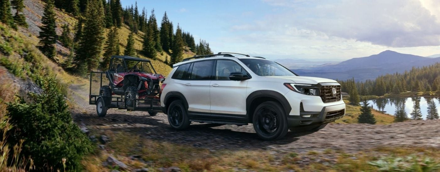 A white 2025 Honda Passport TrailSport towing ATVs on a mountain trail.