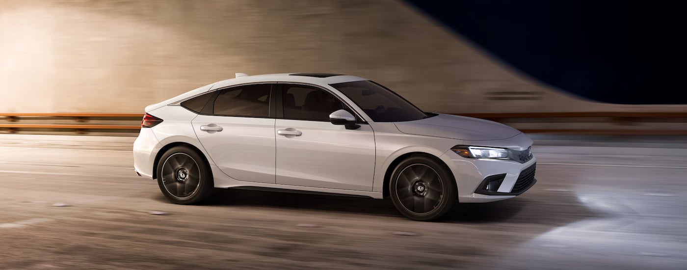 A white 2024 Honda Civic Hatchback Sport Touring driving to a Honda dealer near Brownsburg at night.