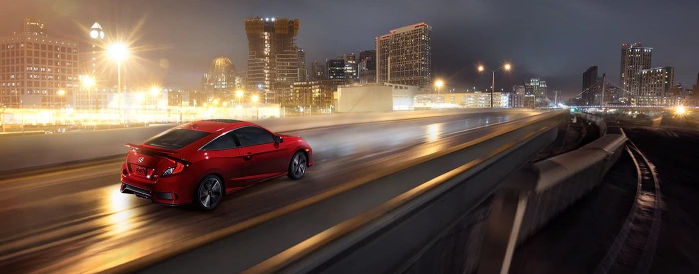 A red 2019 Honda Civic Si is shown driving on a city street at night.