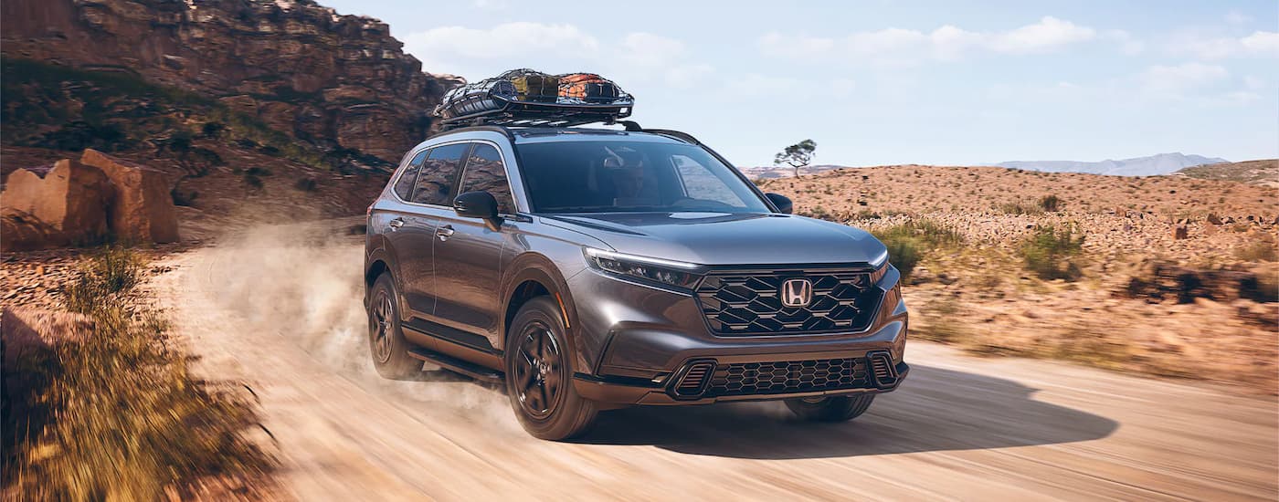 A silver 2024 Honda CR-V Sport Hybrid driving on a dirt road.