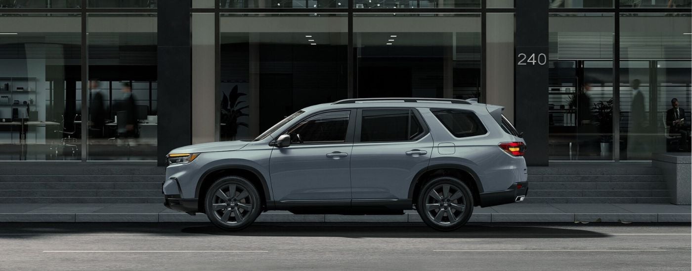 Side view of a silver 2025 Honda Pilot Sport parked on a city street.
