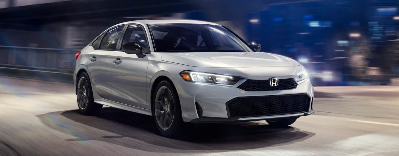 A white 2025 Honda Civic driving in a city from a dealer with a Honda for sale.